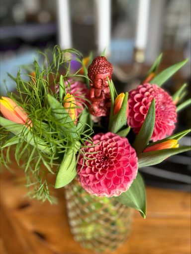 Färgglada blommor i en vas med gröna blad och en liten figur ovanpå.